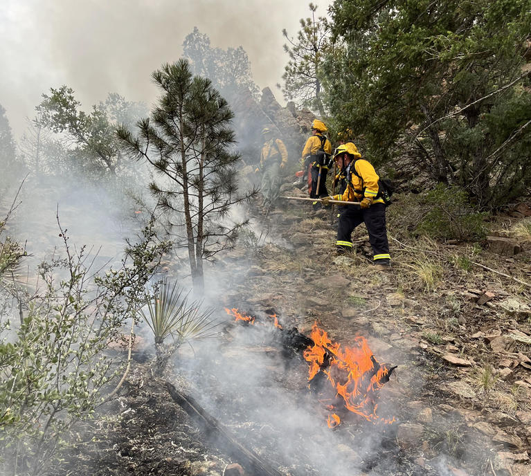 West Metro firefighters on the Snow Creek Fire. The picture shows two firefighters building fire line near some flames. 